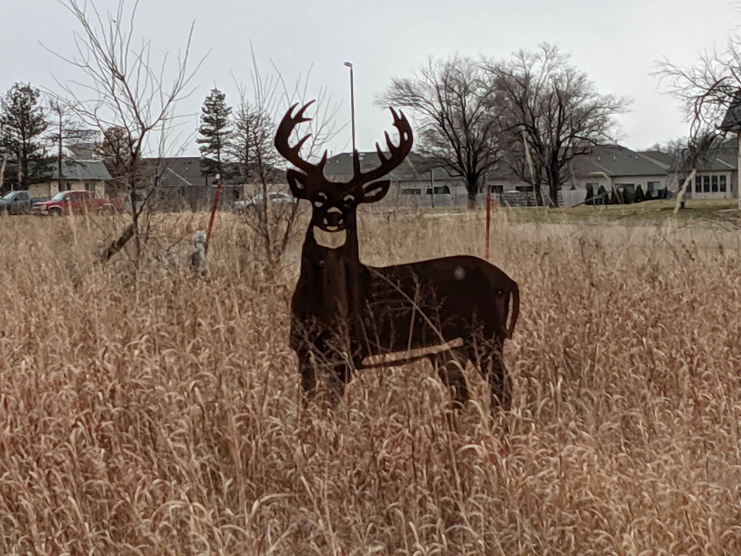 A metal deer sculpture stands gracefully in a field of tall grass